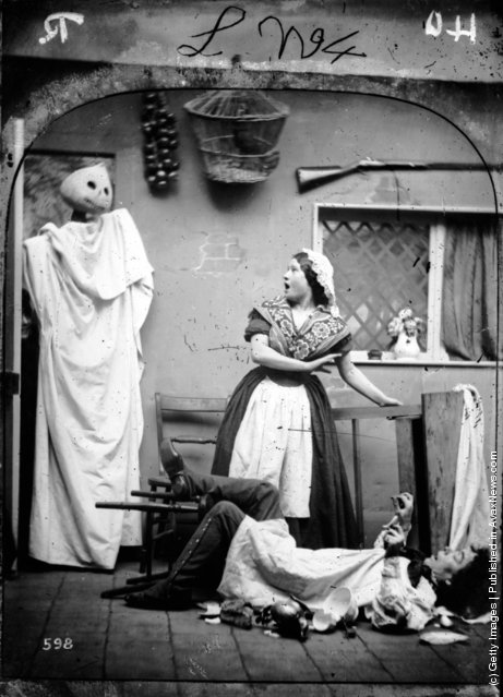 1865: A white caped figure wearing a haloween pumpkin mask taking two people by surprise in their kitchen