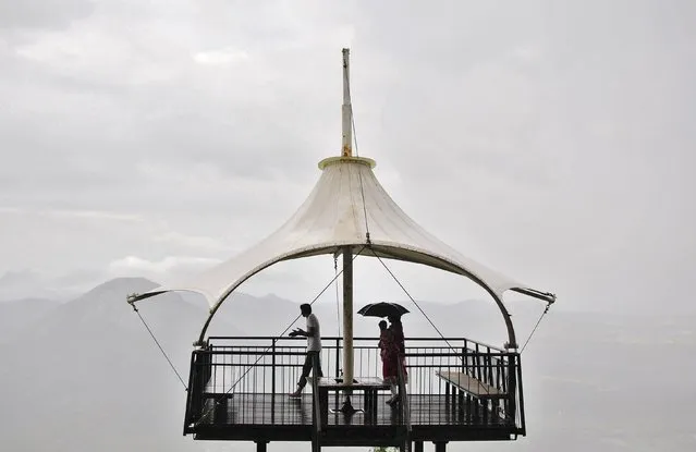 A couple holds a child under the parasol of a watch tower against the backdrop of monsoon clouds on the outskirts of the southern Indian city of Bangalore in this August 11, 2014 file photo. (Photo by Abhishek N. Chinnappa/Reuters)