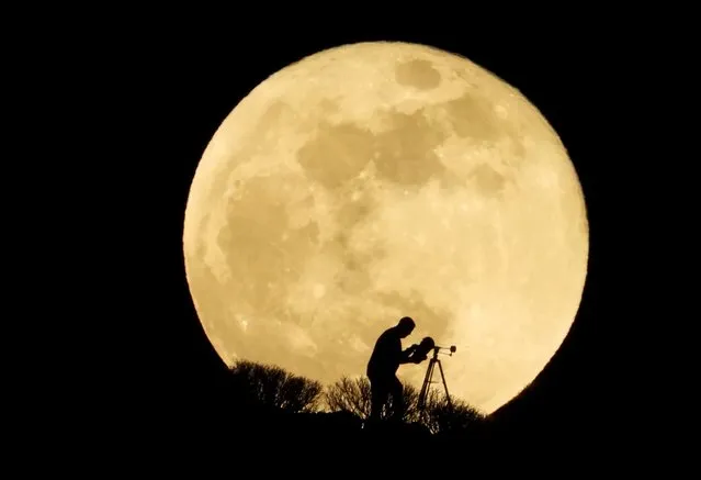 A man uses a telescope to observe the full moon, known as the “Super Flower Moon” as it rises over Arguineguin, in the south of Gran Canaria, Spain on May 26, 2021. (Photo by Borja Suarez/Reuters)