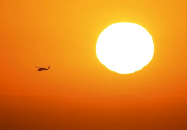 A U.S. military helicopter travels over the pacific ocean past a setting sun near Cardiff, California June 24, 2015. (Photo by Mike Blake/Reuters)