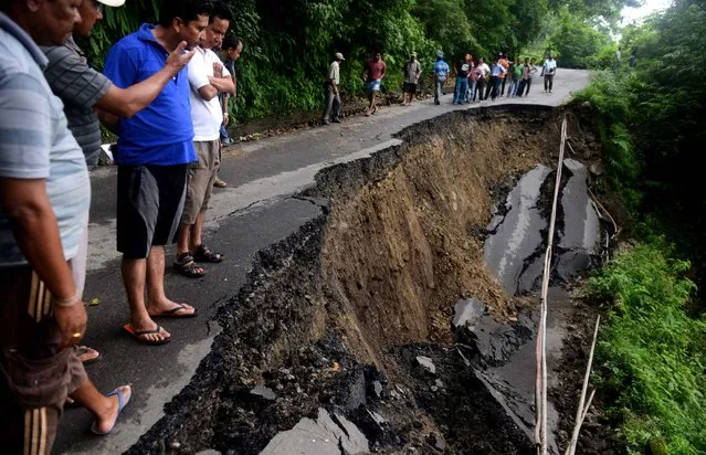 Indian bystanders walk on a landslide affected roadway in the village of Gayabari some 23 kms from Siliguri on July 2, 2015, after landslides struck the eastern state of West Bengal. Landslides triggered by heavy rain killed at least 30 people across India's famed tea-growing region of Darjeeling, with more feared trapped under mounds of mud and debris, police said. (Photo by Diptendu Dutta/AFP Photo)