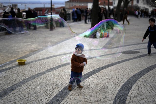 A child watches a street performer making soap bubbles at a public garden in Lisbon, Sunday, February 19, 2023. (Photo by Armando Franca/AP Photo)