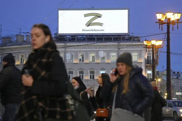 People walk past the letter Z, which has become a symbol of the Russian military, and a hashtag reading “We don't abandon our own” on an advertisement screen in St. Petersburg, Russia, Wednesday, March 9, 2022. (Photo by AP Photo/Stringer)