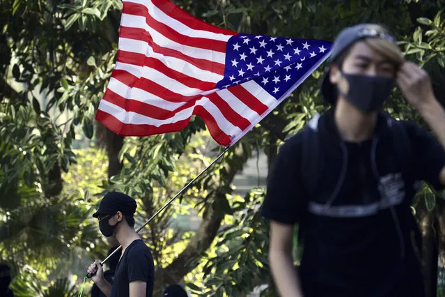A protester waves an American flag during a rally for students and elderly pro-democracy demonstrators in Hong Kong, Saturday, November 30, 2019. Hundreds of Hong Kong pro-democracy activists rallied Friday outside the British Consulate, urging the city's former colonial ruler to emulate the U.S. and take concrete actions to support their cause, as police ended a blockade of a university campus after 12 days. (Photo by Ng Han Guan/AP Photo)