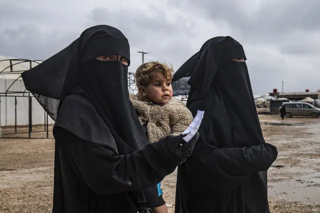 A woman walks carrying a toddler at the Kurdish-run al-Hol camp for the displaced where families of Islamic State (IS) foreign fighters are held, in the al-Hasakeh governorate in northeastern Syria on December 9, 2019. Around 200 Syrian displaced people, mostly women and children, were heading home from an overcrowded desert camp in the northeast of the war-torn country on December 8, a Kurdish official said. The majority were civilians with no ties to IS, he said, while a few might have aligned with the jihadists but today regretted their decision. (Photo by Delil Souleiman/AFP Photo)