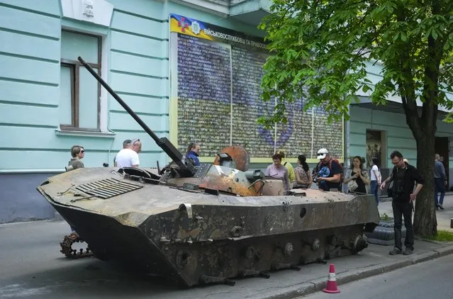 People look at a Russian military vehicle destroyed by the Ukrainian troops in a battle against the Russian invaders and taken to the capital as a reminder of war in Kyiv, Ukraine, Thursday, May 12, 2022. (Photo by Efrem Lukatsky/AP Photo)