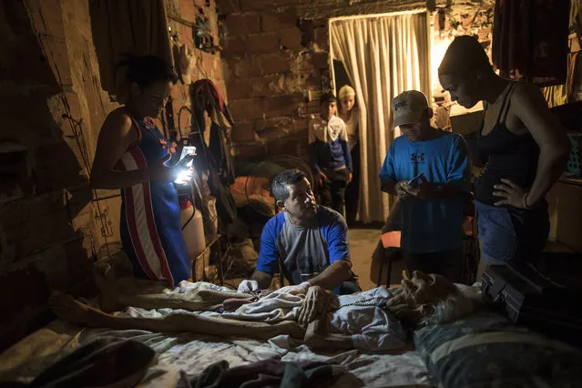 Community activist Carolina Leal uses a cell phone to light up the work area for Roberto Molero as he prepares the body of Teresa Jimenez, 91, after she died of natural causes in her home in Maracaibo, Venezuela, November 17, 2019. Molero embalms bodies with no training other than seeing it done during a decade that he work as a driver at a funeral home, while Leal assumes the role of funeral director in her poor and often violent Maracaibo neighborhood, hoping to rid families of unnecessary misery she's seen too many times. (Photo by Rodrigo Abd/AP Photo)