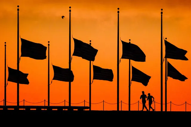 Runners pass under the the flags flying at half-staff around the Washington Monument at daybreak in Washington, Monday, June 13, 2016. The flags were ordered to half-staff by President Barack Obama to honor the victims of the Orlando nightclub shootings. (Photo by J. David Ake/AP Photo)