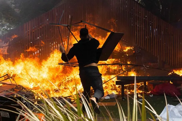A man throws a desk onto a fire that rages on the grounds in front of Parliament as police move in to clear protesters in Wellington on March 2, 2022, on day twenty three of demonstrations against Covid-19 vaccine mandates and restrictions. (Photo by Marty Melville/AFP Photo)