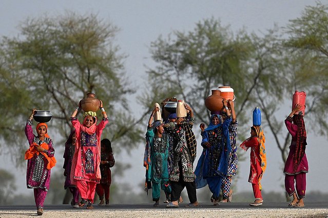 In this picture taken on May 11, 2022, women walk towards their homes carrying drinking water in containers during heatwave in the outskirts of Jacobabad, in southern Sindh province. (Photo by Aamir Qureshi/AFP Photo)