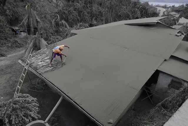 A resident clears volcanic ash from his roof in Laurel, Batangas province, southern Philippines on Tuesday, January 14, 2020. Taal volcano is spewing ash half a mile high and trembling with earthquakes constantly as thousands of people flee villages darkened and blanketed by heavy ash. (Photo by Aaron Favila/AP Photo)