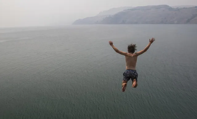 Eli Garlick jumps into Lake Kalamalka in Vernon, British Columbia, Monday, July 17, 2017. The Okanagan area is blanketed with smoke from wildfires burning in the interior of the province. (Photo by Jeff Bassett/The Canadian Press via AP Photo)