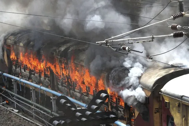 Flames rise from a train set on fire by protestorsat Secundrabad railroad station in Hyderabad, India, Friday, June 17, 2022. Hundreds of angry youths gave vent to their ire by burning train coaches, vandalizing railroad property and blocking rail tracks and highways with boulders as a backlash continued for a second straight day Friday against a new short-term government recruitment scheme for the military. Nearly 500 protesters vastly outnumbered policemen as they went on a rampage for more than an hour at Secundrabad railroad station in southern India. (Photo by Mahesh Kumar A./AP Photo)