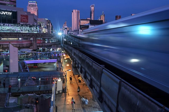 Pedestrians use the skywalk bridge between shopping malls as BTS trains pass above them in Bangkok on October 16, 2024. (Photo by Lillian Suwanrumpha/AFP Photo)