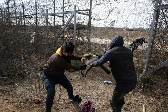 Migrants try to cut the fence at the Turkish-Greek border during clashes with the Greek police near the Pazarkule border gate in Edirne, Turkey on Monday, March 2, 2020. Thousands of migrants and refugees massed at Turkey's western frontier, trying to enter Greece by land and sea after Turkey said its borders were open to those hoping to head to Europe. (Photo by Darko Bandic/AP Photo)