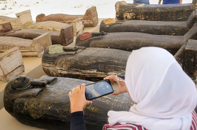 A reporter films painted coffins with well-preserved mummies inside, dating back to the Late Period of ancient Egypt around 500 B.C, displayed during a press conference at a makeshift exhibit at the feet of the Step Pyramid of Djoser in Saqqara, 24 kilometers (15 miles) southwest of Cairo, Egypt, Monday, May 30, 2022. (Photo by Amr Nabil/AP Photo)