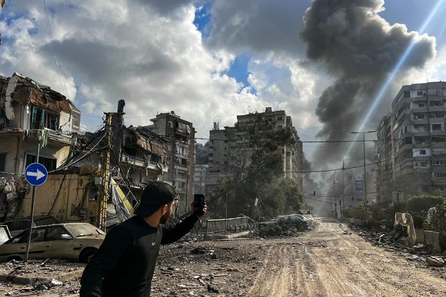 A man uses his mobile phone to take photos as smoke rises from the site of an Israeli airstrike targeting a neighborhood in southern Beirut on November 13, 2024, amid the ongoing war between Israel and Hezbollah. (Photo by Ibrahim Amro/AFP Photo)