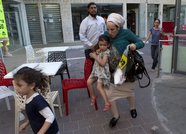 A religious Israeli family running across a parking area towards a shelter among some shops in the southern Israeli town of Sderot as a “red alert” siren sounds, 21 August 2014, signaling a rocket attack launched from the Gaza Strip is heading towards this border community. The young girl fell and the mother picked her up and carried her into the shelter. (Photo by Jim Hollander/EPA)