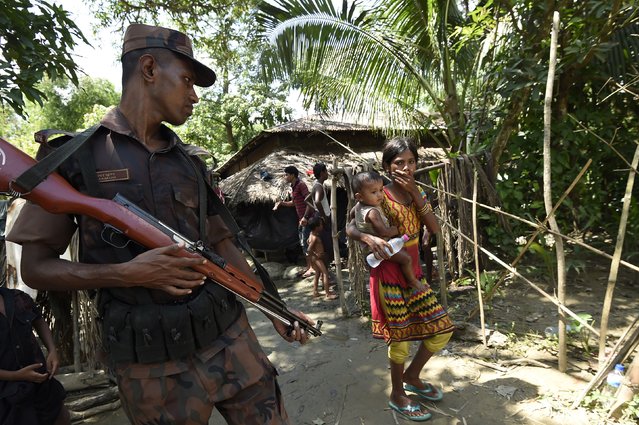 This September 16, 2017 photo shows a Bangladesh border guard looking at Rohingya refugees at the Jalpatoli refugee camp in the no-man's land area between Myanmar and Bangladesh, near Gumdhum village in Ukhia. More than 400,000 Rohingya Muslims have now arrived in southern Bangladesh seeking sanctuary from violence that the United Nations says likely amounts to ethnic cleansing. But unlike those arriving now, thousands of Rohingya who fled in the early days of the crisis that erupted last month were initially blocked from entering Bangladesh. Too afraid to go back to Myanmar, they set up camp in a small area of no man's land where they have been ever since, waiting for the world to force the country they consider home to take them back. (Photo by Dominique Faget/AFP Photo)