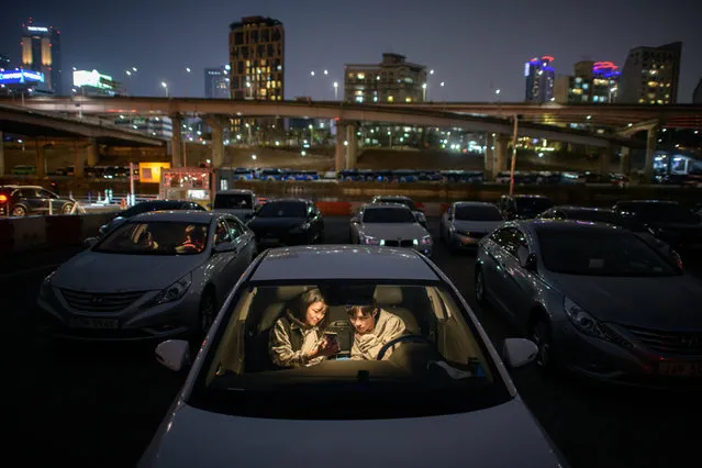 In a photo taken on March 21, 2020 a couple look at a mobile phone as they sit in a car at a screening at a drive-through cinema in Seoul. Box office numbers in South Korea – which has 8,897 confirmed virus cases – have plummeted in recent weeks due to the epidemic, with authorities urging the public to avoid large crowds. But at drive-in cinemas, moviegoers can enjoy a movie from the comfort of their cars, parked in front of a large outdoor screen. (Photo by Ed Jones/AFP Photo)