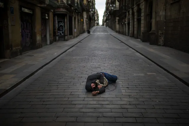 A man sleeps in an empty street during the coronavirus outbreak in Barcelona, Spain, Friday, April 17, 2020. (Photo by Emilio Morenatti/AP Photo)