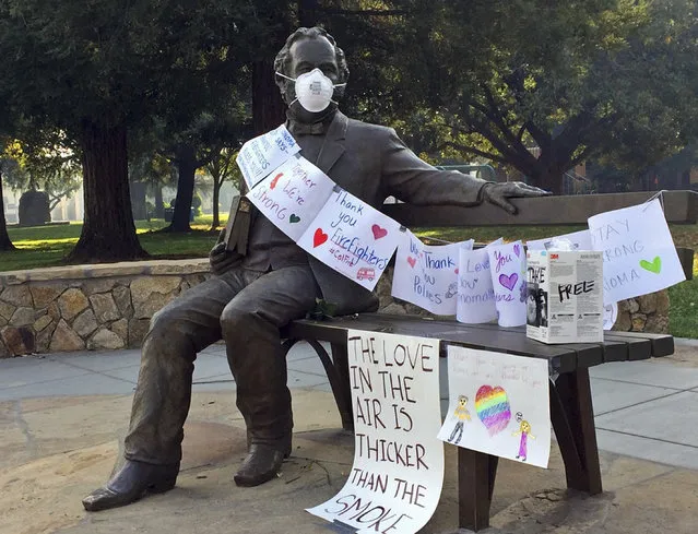 In the historic main square of the wine and tourist town of Sonoma, Calif., townspeople have rigged a statue of the town's 19th century founder, Gen. Mariano Vallejo, with a face mask and signs thanking firefighters, seen Monday, October 16, 2017. Vallejo's statue was presiding over a main square empty of the picnickers, playing children and tourists who normally fill it. Power outages, evacuation orders and advisories, and active fires in the ridges over town were still shutting down most of the town of 11,000. (Photo by Ellen Knickmeyer/AP Photo)