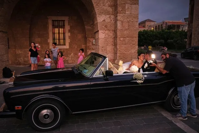 A photographer takes pictures of a newly wedded couple in a classic car, in front of the Saint Estephan Maronite church at the fishermen's port of the northern Lebanese city of Batroun, on August 6, 2022. (Photo by Ibrahim Chalhoub/AFP Photo)