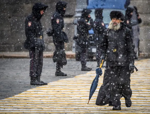 An Orthodox priest walks past a police line blocking the access to Red Square during a rehearsal for the upcoming parade, Moscow, October 26, 2017. The event will take place on November 7, marking the 76th anniversary of the 1941 historical parade, when Red Army soldiers marched past the Kremlin walls towards the front line to fight the Nazi Germany troops during World War Two. (Photo by Mladen Antonov/AFP Photo)