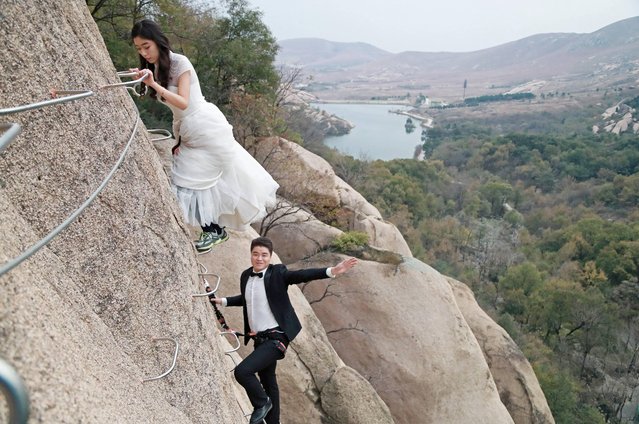 A newlywed couple dangling from a cliff face poses for wedding photos at the Chaya Mountain scenic spot on November 11, 2017 in Zhumadian, Henan Province of China. (Photo by Sipa Asia/Rex Features/Shutterstock)