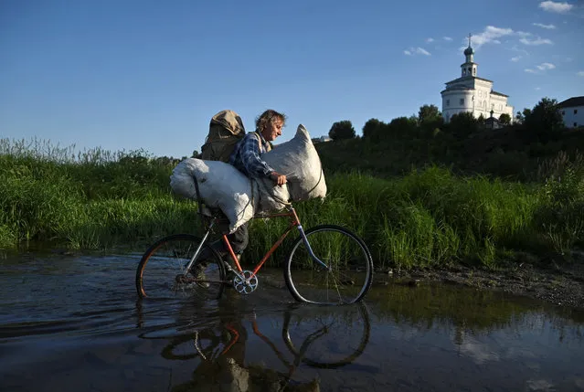 A man pushes a bicycle through the water as he returns after mowing a field in the town of Cherdyn in Perm Region, Russia on July 12, 2020. (Photo by Alexey Malgavko/Reuters)