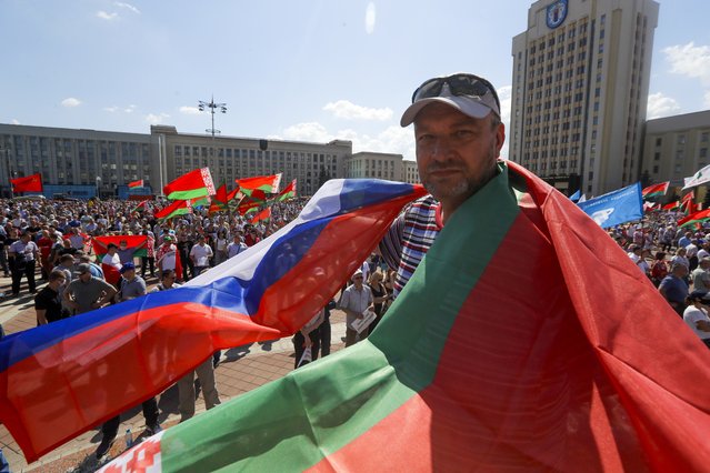 A man covers himself with Belarusian State and Russian national flags as supporters of Belarusian President Alexander Lukashenko gather at Independent Square of Minsk, Belarus, Sunday, August 16, 2020. Thousands of people have gathered in a square near Belarus' main government building for a rally to support President Alexander Lukashenko, while opposition supporters whose protests have convulsed the country for a week aim to hold a major march in the capital. (Photo by Sergei Grits/AP Photo)