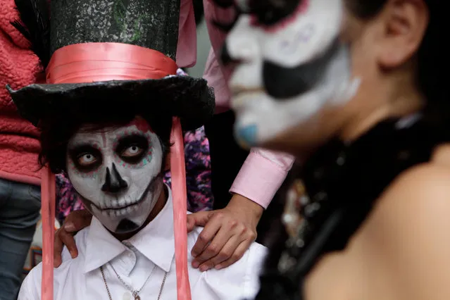 Angel Paz, dressed as a calavera, waits with family for the start of the Gran Procession of the Catrinas, to mark the upcoming Day of the Dead holiday, in Mexico City, Sunday, October 23 2016. (Photo by Anita Baca/AP Photo)