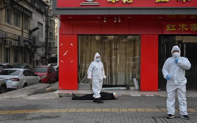 This photo taken on January 30, 2020 shows officials in protective suits checking on an elderly man wearing a facemask who collapsed and died on a street near a hospital in Wuhan. AFP journalists saw the body on January 30, not long before an emergency vehicle arrived carrying police and medical staff in full-body protective suits. The World Health Organization declared a global emergency over the new coronavirus, as China reported on January 31 the death toll had climbed to 213 with nearly 10,000 infections. (Photo by Hector Retamal/AFP Photo)