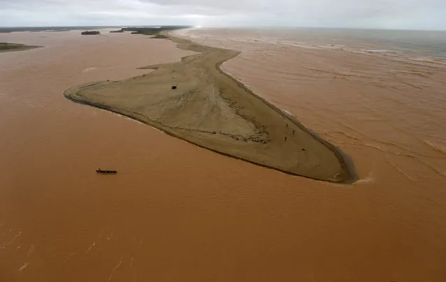 A boat is seen on the mouth of Rio Doce (Doce River), which was flooded with mud after a dam owned by Vale SA and BHP Billiton Ltd burst, as the river joins the sea on the coast of Espirito Santo in Regencia Village, Brazil, November 22, 2015. (Photo by Ricardo Moraes/Reuters)