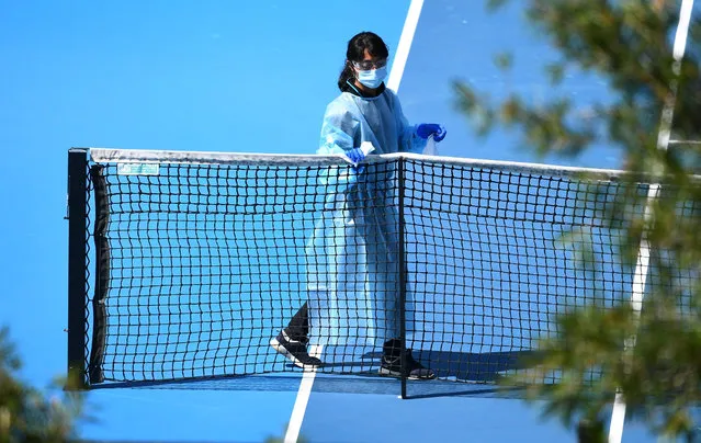 A cleaner wipes down the nets as she prepares the court for the next group of tennis players for a practice session in Melbourne on January 21, 2021, with players allowed to train while on quarantine for two weeks ahead of the Australian Open tennis tournament. (Photo by William West/AFP Photo)