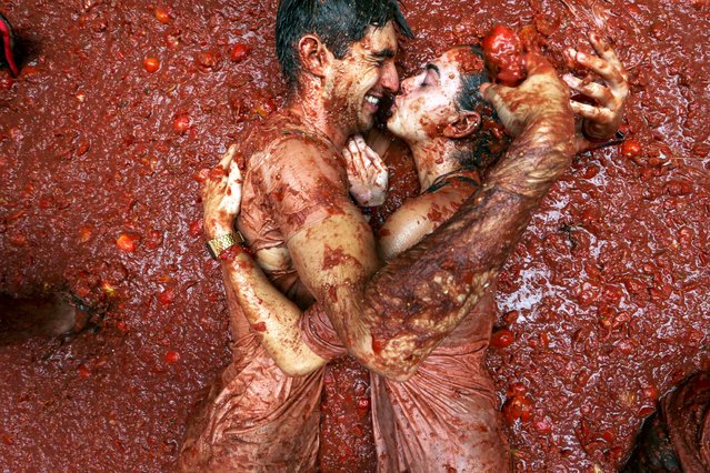 Revelers embrace in a pool of squashed tomatoes during the annual “Tomatina” tomato fight fiesta, in Bunol, Spain, August 28, 2024. (Photo by Alberto Saiz/AP Photo)
