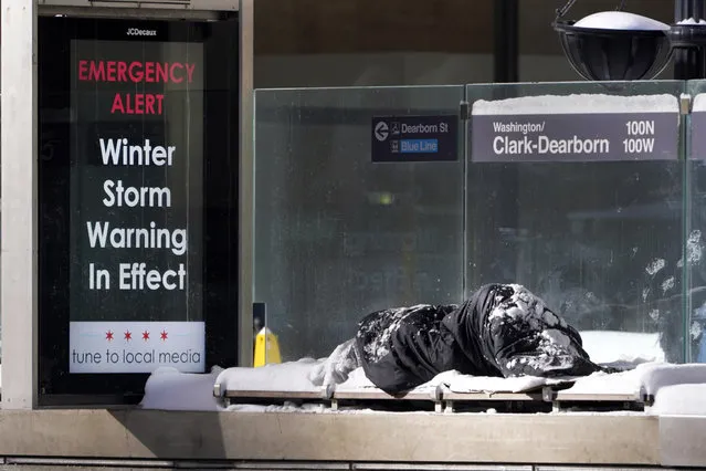 A homeless man Tuesday, February 16, 2021, sleeps at the Chicago Transit Authority's Clark & Dearborn bus station, the morning after a snowstorm dumped up to 18 inches in the greater Chicago area. (Photo by Charles Rex Arbogast/AP Photo)