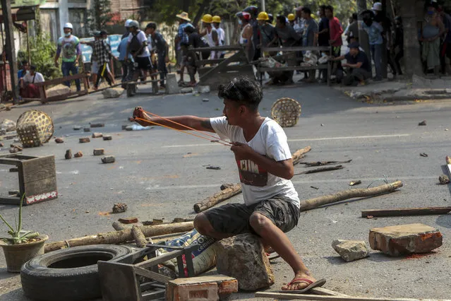 An anti-coup protester uses a sling-shot and against advancing riot policemen in Mandalay, Myanmar, Tuesday, March 2, 2021. (Photo by AP Photo/Stringer)