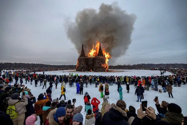 This picture taken on March 13, 2021, shows spectators watching the burning wooden structure 'Corona Tower' created by Russian artist Nikolay Polissky during celebrations of Maslenitsa, the eastern Slavic Shrovetide in the village of Nikola-Lenivets. Shrovetide or Maslenitsa is an ancient farewell ceremony to winter, traditionally celebrated in Belarus, Russia and Ukraine and involves the burning of a large effigy. (Photo by Dimitar Dilkoff/AFP Photo)