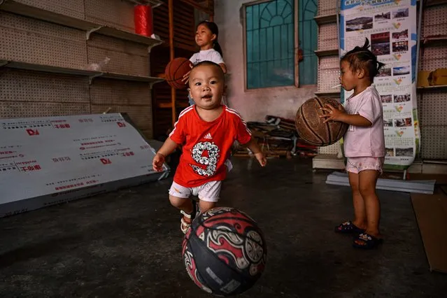 This photo taken on July 30, 2023 children playing with basketballs at an empty store in Taipan village where a CunBA grassroots basketball competition is held, in Taijiang county, southwestern China's Guizhou province. Athletes in the “CunBA” – with “cun” meaning village in Chinese – are all amateurs, and the prizes are simple platters of roast meat. But it's the pure electricity of the games that keeps fans and players hooked, rising in recent years from a humble local tradition into a viral hit and staple of Beijing's propaganda machine. (Photo by Jade Gao/AFP Photo)