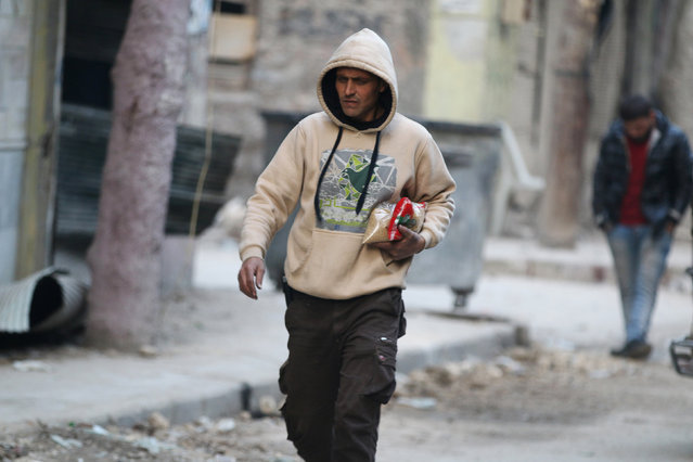 A man carries food as he walks along a street in a rebel-held besieged area of Aleppo, Syria December 10, 2016. (Photo by Abdalrhman Ismail/Reuters)