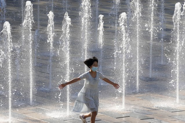 A girl wearing a mask to help curb the spread of the corona virus runs through a fountain in Beijing, China, Thursday, August 26, 2021. (Photo by Ng Han Guan/AP Photo)