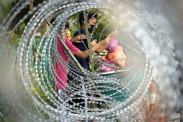 Residents receive food from a delivery man through barbwire at Segambut Dalam area placed under the enhanced movement control order (EMCO) due to drastic increase in the number of COVID-19 cases recorded in Kuala Lumpur, Malaysia, Sunday, July 4, 2021. Malaysia starts further tightening movement curbs and imposes a curfew in most areas in its richest state Selangor and parts of Kuala Lumpur, where coronavirus cases remain high despite a national lockdown last month. (Photo by Vincent Thian/AP Photo)