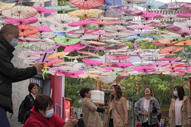 Women share a light moment as visitors wearing face masks take picture underneath colorful umbrellas on display along a hutong alley near Qianmen Avenue, a popular tourist spot in Beijing, Thursday, October 14, 2021. (Photo by Andy Wong/AP Photo)
