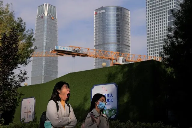 A woman holding a face mask yawns while passing by a construction crane at the Central Business District in Beijing, Monday, October 18, 2021. China's economic growth sank in the latest quarter as a slowdown in construction and curbs on energy use weighed on its recovery from the coronavirus pandemic. (Photo by Andy Wong/AP Photo)