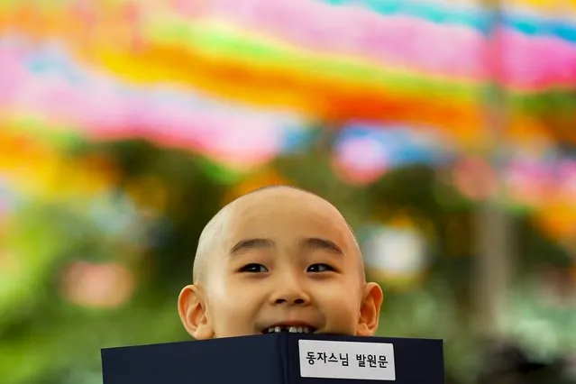A novice monk holds a book during an inauguration ceremony at Jogye temple in Seoul, May 11, 2015. Ten children on Monday were given the opportunity to experience life as Buddhist monks by staying at the temple until Buddha's birthday in two weeks. The writing on the book reads, “Novice Monk Prayer”. (Photo by Thomas Peter/Reuters)