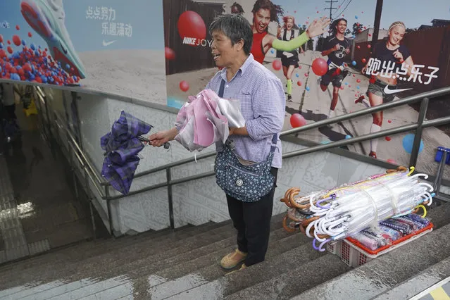 A woman sells umbrella at a subway entrance as Typhoon Lekima approaches in Shanghai  Saturday, August 10, 2019. Typhoon Lekima has struck China's coast south of Shanghai, knocking down trees and forcing airlines to cancel flights. (Photo by Erika Kinetz/AP Photo)