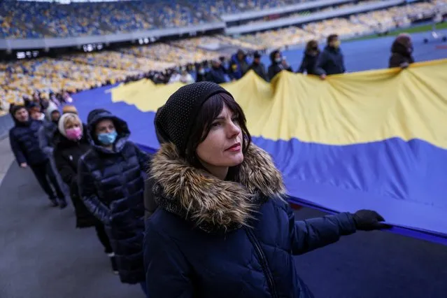 Residents carry Ukrainian national flag as they gather in the Olympic Stadium to mark the Unity Day, the day Western intelligence agencies allegedly said they'd be invaded by Russia, in Kyiv, Ukraine, February 16, 2022. (Photo by Umit Bektas/Reuters)