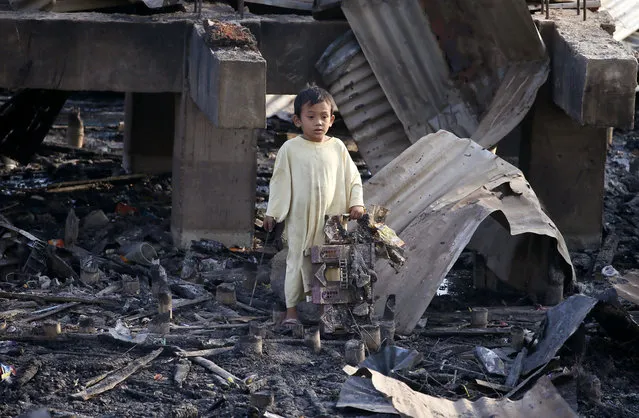 A boy holds a burnt doll house he sifted through the debris following an overnight fire that razed through a coastal village in Bacoor township, Cavite province southwest of Manila, Philippines Thursday, April 6, 2017. Fire authorities are still investigating the cause of the fire that damaged more than 600 houses and rendered homeless to more than a thousand families. (Photo by Bullit Marquez/AP Photo)