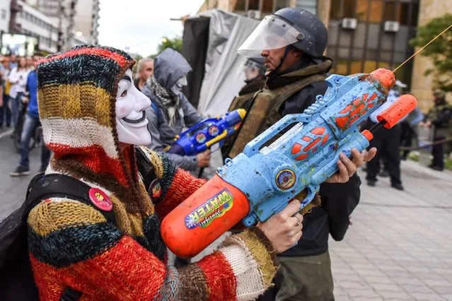 Masked protestors use water guns filled with paint on the Public Revenue Office building, being guarded by police officers, during the protest dubbed “Colorful  Revolution” against Macedonian President Ivanov's decision on wiretapping amnesty, in Skopje, The Former Yogoslav Republic of Macedonia, 10 May 2016. Protests in Macedonia continue daily for almost three weeks, after the decision of the president George Ivanov  to pardon dozens of politicians who were involved in wiretapping scandal. (Photo by Georgi Licovski/EPA)